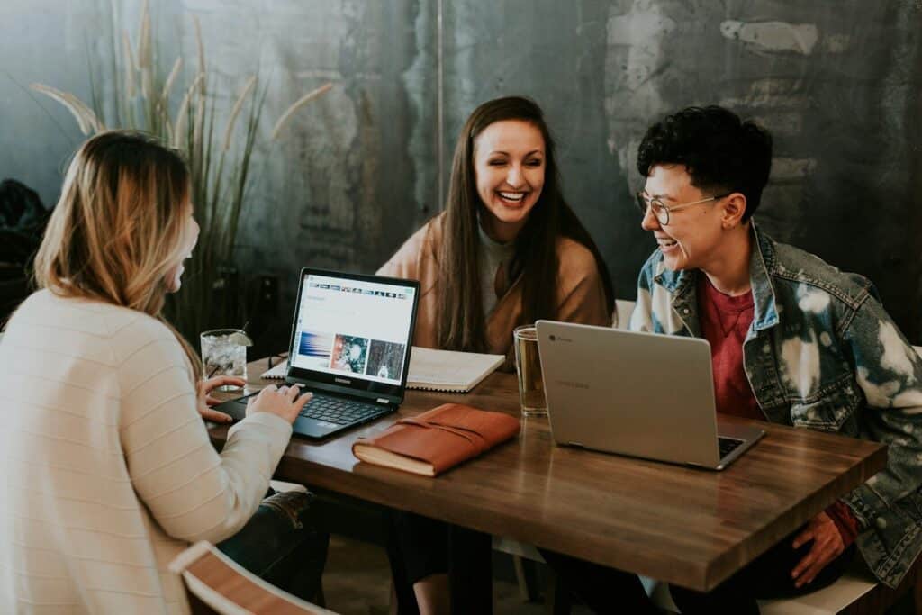 Drei junge Menschen arbeiten gemeinsam an einem Tisch mit Laptops und Unterlagen – Sinnbild für Ausbildung, Teamarbeit und Wissensaustausch.