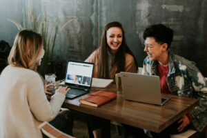 Drei junge Menschen arbeiten gemeinsam an einem Tisch mit Laptops und Unterlagen – Sinnbild für Ausbildung, Teamarbeit und Wissensaustausch.